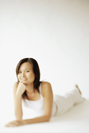 Young woman lying on floor, hands on chin, looking at cameraの写真素材