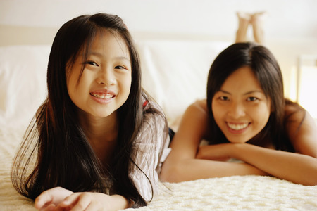 Mother and daughter lying on bed, looking at cameraの写真素材