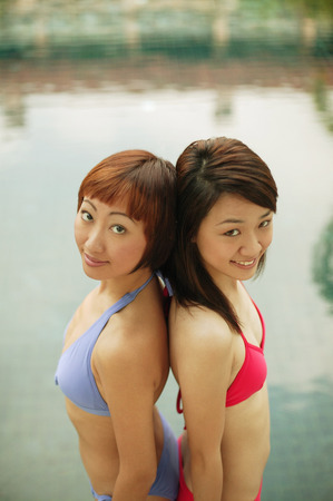 Two young women, standing back to back, smilingの写真素材