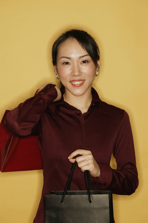 Young woman carrying shopping bags, yellow backgroundの写真素材