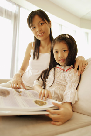 Mother and daughter, sitting side by side, looking at camera, smilingの写真素材