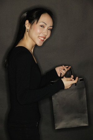 Young woman carrying shopping bag, black backgroundの写真素材