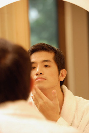 Young man  looking in mirror, touching his faceの写真素材