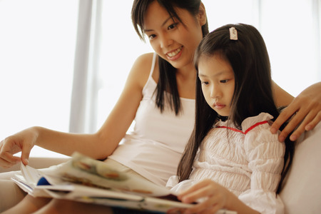 Mother and daughter, sitting side by side, looking at bookの写真素材