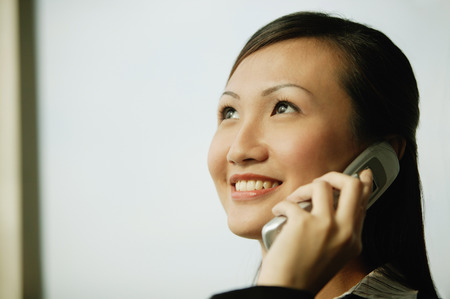 Young woman on mobile phone, looking up, smilingの写真素材