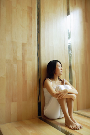 Young woman sitting, hugging knees, looking upの写真素材