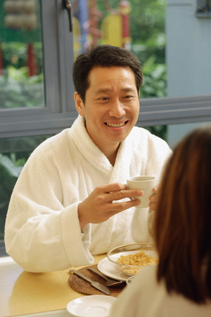 Couple facing each other, holding cups of coffee, man smilingの写真素材