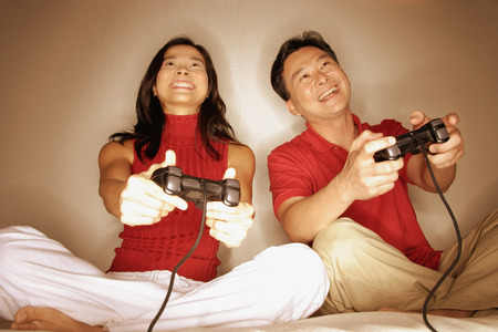 Man and woman playing with handheld video game, looking forwardの写真素材
