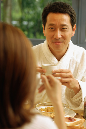 Couple facing each other, holding cups of coffeeの写真素材
