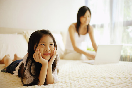 Mother and daughter in bedroom, mother using laptopの写真素材