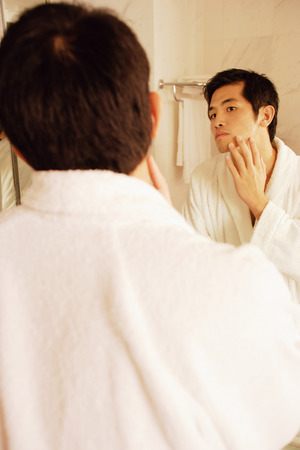 Young man touching his face, looking in mirror, rear viewの写真素材