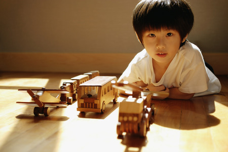 Young boy looking at camera, toys in a row in front of himの写真素材