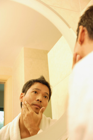 Young man touching his face, looking in mirrorの写真素材