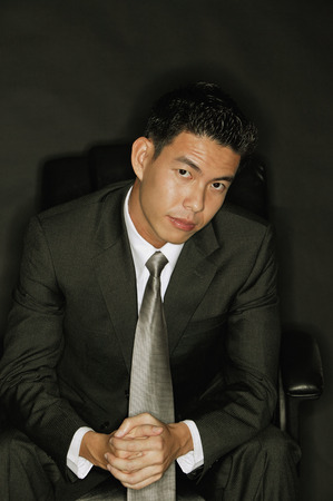 Young man looking at camera, hands claspedの写真素材