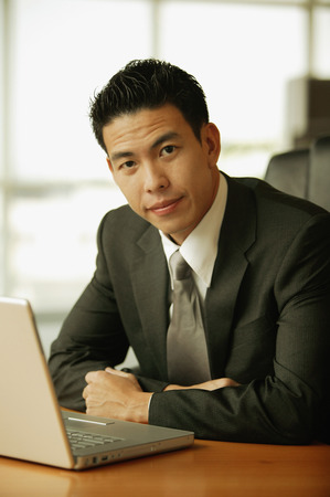 Young man looking at camera, laptop open on the tableの写真素材