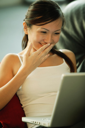 Young woman on sofa, using laptop, smilingの写真素材