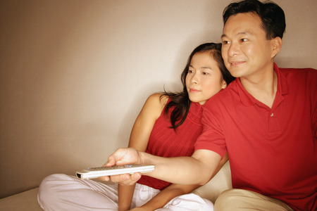 Man and woman sitting side by side, man with remote controlの写真素材