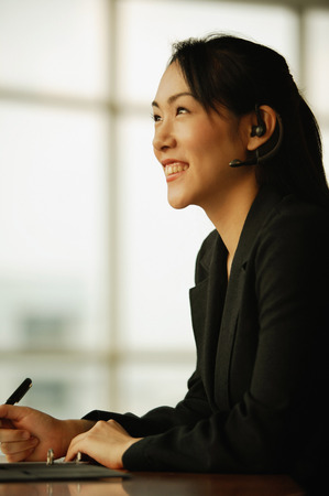 Young woman sitting at desk, using hands-free deviceの写真素材