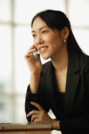Young woman sitting at desk, using mobile phoneの写真素材