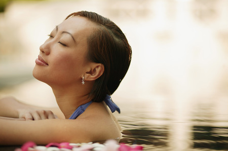 Young woman, at edge of swimming pool, head tilted up.の写真素材