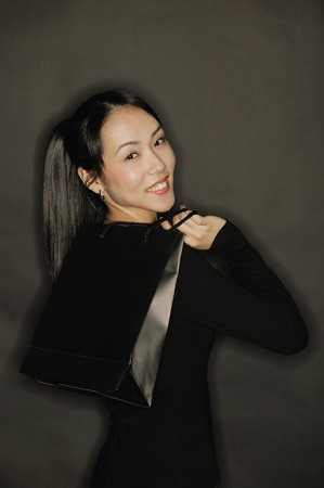 Young woman carrying shopping bag, black backgroundの写真素材