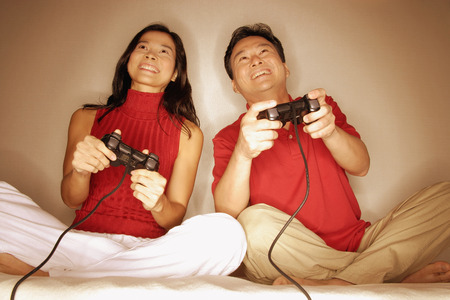Man and woman sitting side by side, legs crossed, playing with handheld video gameの写真素材