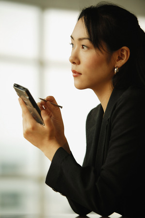 Young woman sitting at desk, using PDAの写真素材