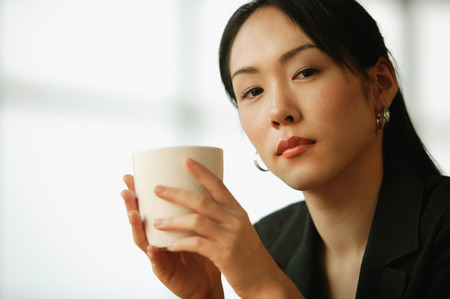 Young woman sitting at desk, holding mugの写真素材