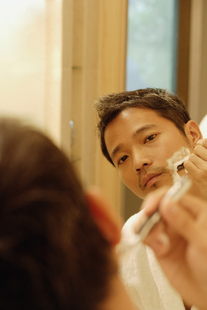 Young man shaving, looking in mirrorの写真素材