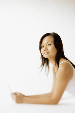 Young woman lying on floor, holding mobile phone, looking at cameraの写真素材