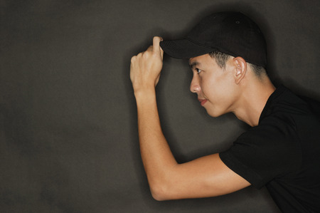Young man touching cap, black backgroundの写真素材