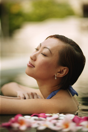 Young woman, at edge of swimming pool, head tilted up.の写真素材