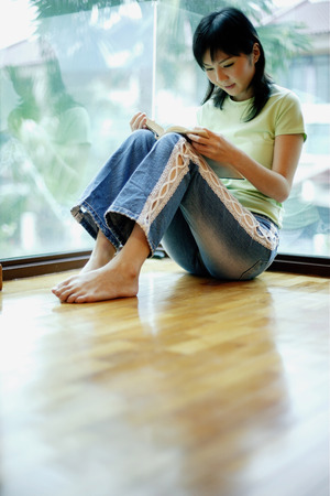 Woman leaning on window, reading a bookの写真素材