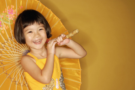 Young girl standing against yellow background, holding umbrella, laughingの写真素材