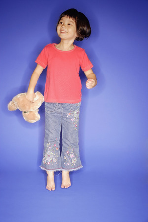 Young girl jumping, holding teddy bearの写真素材