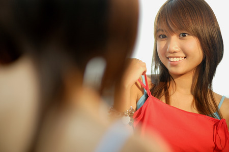 Young woman looking at mirror, holding up tank topの写真素材
