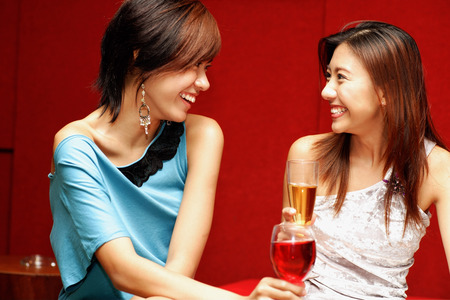 Two young women, with drinks, facing each otherの写真素材