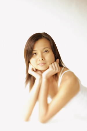 Young woman lying on floor, hands on chin, looking at cameraの写真素材