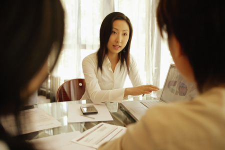 Young female executive using laptop, presenting to colleaguesの写真素材