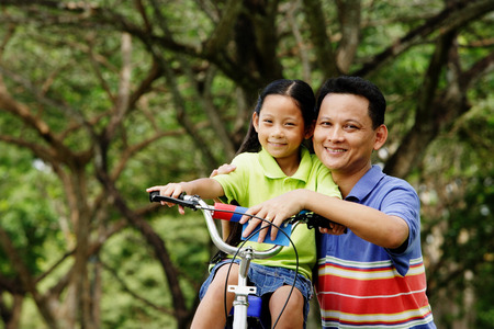Girl on bicycle, father next to her, both looking at cameraの写真素材