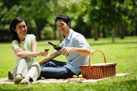 Couple in park, man pouring wine for woman, both looking at cameraの写真素材