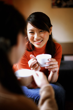 Two young women drinking from cups, face to face, over the shoulder viewの写真素材