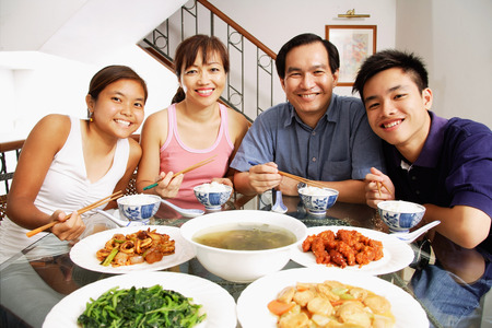 Family at home, sitting side by side, looking at camera, food on the tableの写真素材