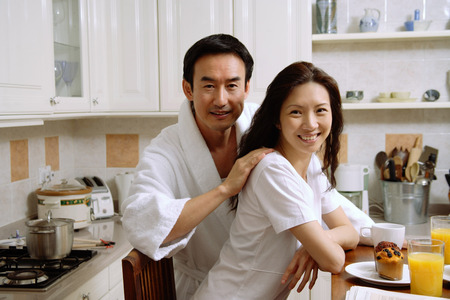 Couple sitting in kitchen, smiling at cameraの写真素材