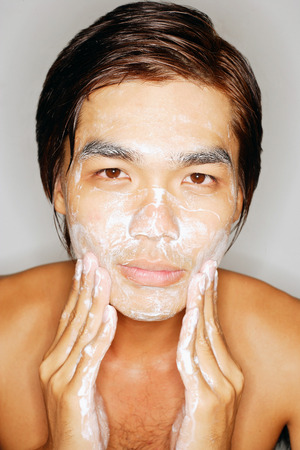 Young man washing face, looking at cameraの写真素材