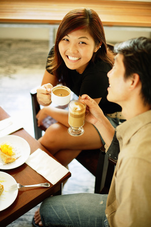 Couple at cafe, holding cups of coffee, woman looking up at cameraの写真素材