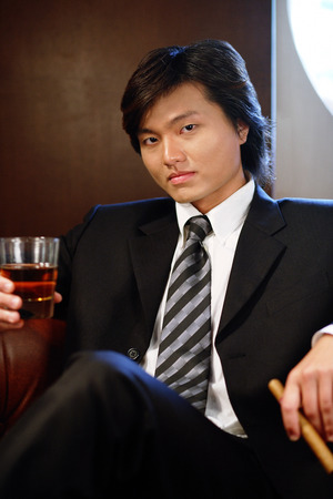 Businessman holding glass and cigar, looking at camera, portraitの写真素材