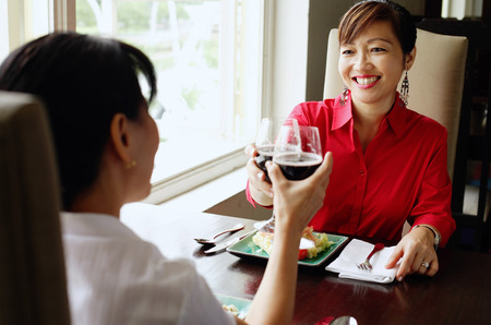 Two women at restaurant, toasting with wine glasses