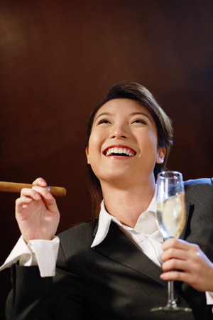 Businesswoman with glass of champagne and cigar, looking up,の写真素材