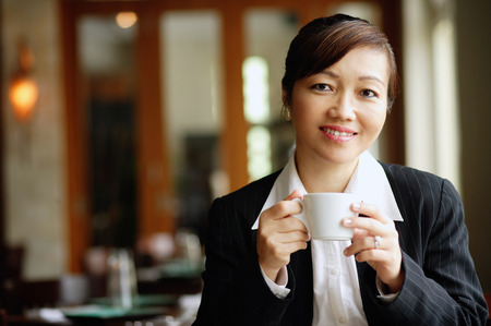 Businesswoman in restaurant, holding cup, looking at cameraの写真素材